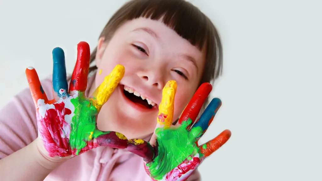 A girl with downs syndrome showing off her paint colored fingers