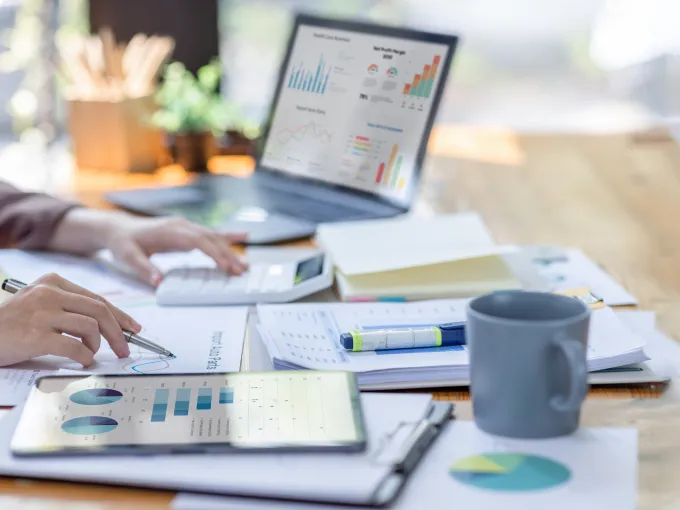 Person at desk with computer, calculator, and papers with charts